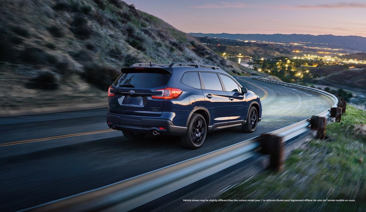Subaru Ascent bleu foncé vu de trois quarts arrière en conduite sur une route sinueuse de montagne au crépuscule.